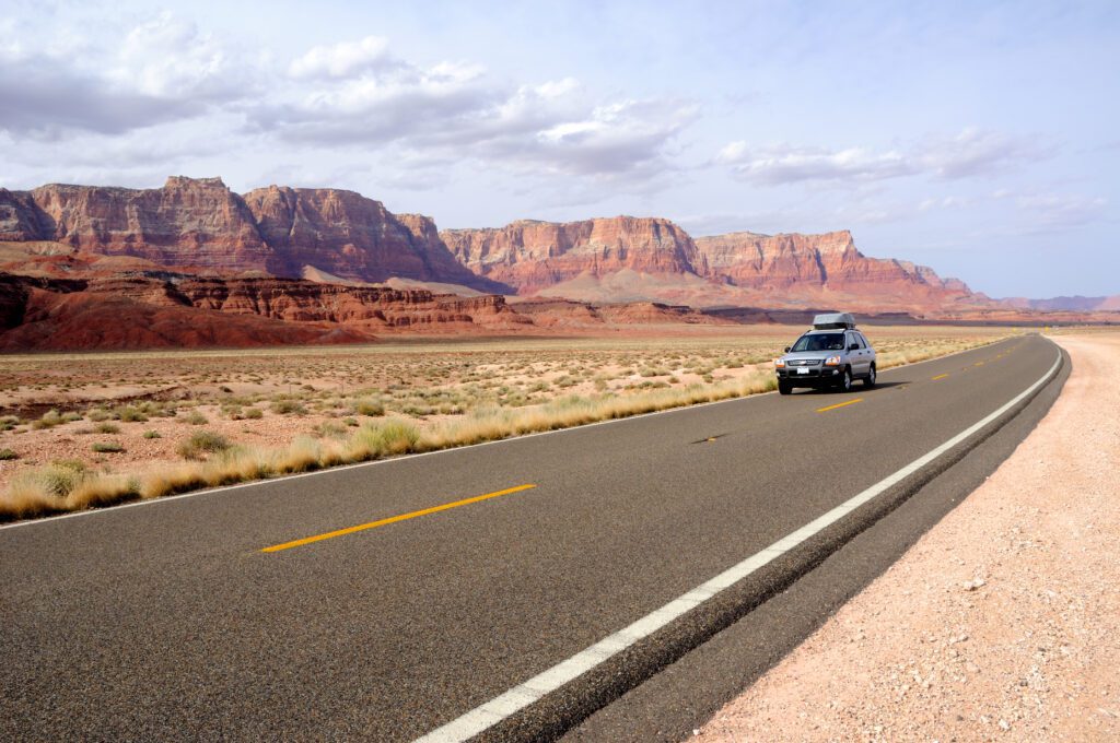 Silver SUV driving on scenic Highway 89A past the red sandstone formations of Vermilion Cliffs in Arizona.